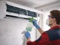 Profesjonalne odgrzybianie klimatyzacji w domu. Mężczyzna w masce i rękawiczkach dezynfekuje urządzenie.