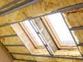 Ocieplenie poddasza z wełny mineralnej w trakcie montażu. Widać okna dachowe i metalowy stelaż.