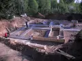 Budowa fundamentów domu. Wykop, zbrojenie i szalunki. W tle las, pracują dwaj chudziaki.