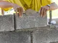 Ręce murarza układają bloczki betonowe fundamentowe, tworząc solidną podstawę.