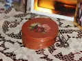 Okrągłe pudełko ozdobione techniką decoupage z motywem róż. Obok broszka i ramka ze zdjęciem.