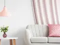 Jasna kanapa z różową poduszką, obok stolik z bukietem białych róż w wazonie. W tle zasłony w kolorze brzoskwiniowym.