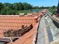 Trwa wymiana dachu. Stare dachówki są ułożone w stosy, a pod nimi widać izolację i drewniane elementy konstrukcji.