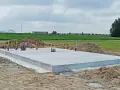 Solidny fundament czeka na budowę domu. Wokół piasek i zielone pola.