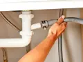 Ręka podłącza wąż odpływowy zmywarki do syfonu pod zlewem.