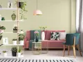 Salon z różową kanapą, zielonymi akcentami i roślinami. Ściany w subtelnym kolorze pistacjowym tworzą przytulną atmosferę.