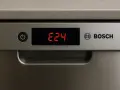 Wyświetlacz zmywarki Bosch pokazuje błąd E24. Czerwone cyfry E24 na czarnym tle obok przycisku zasilania.