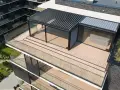 Nowoczesny taras na dachu z przeszklonym pawilonem i pergolą. Drewniana deska tarasowa i szklane balustrady tworzą elegancką przestrzeń.