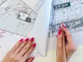 Ręka z różowymi paznokciami wskazuje ołówek na mapie do celów projektowych, gdzie widoczne są plany budowy i przyłączy.