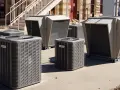 Kilka jednostek klimatyzacyjnych, w tym klimatyzacja kanałowa, stoi na zewnątrz budynku.