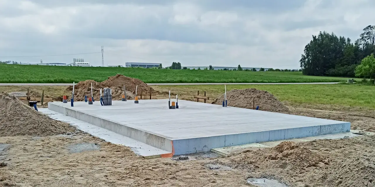 Solidny fundament czeka na budowę domu. Wokół piasek i zielone pola.