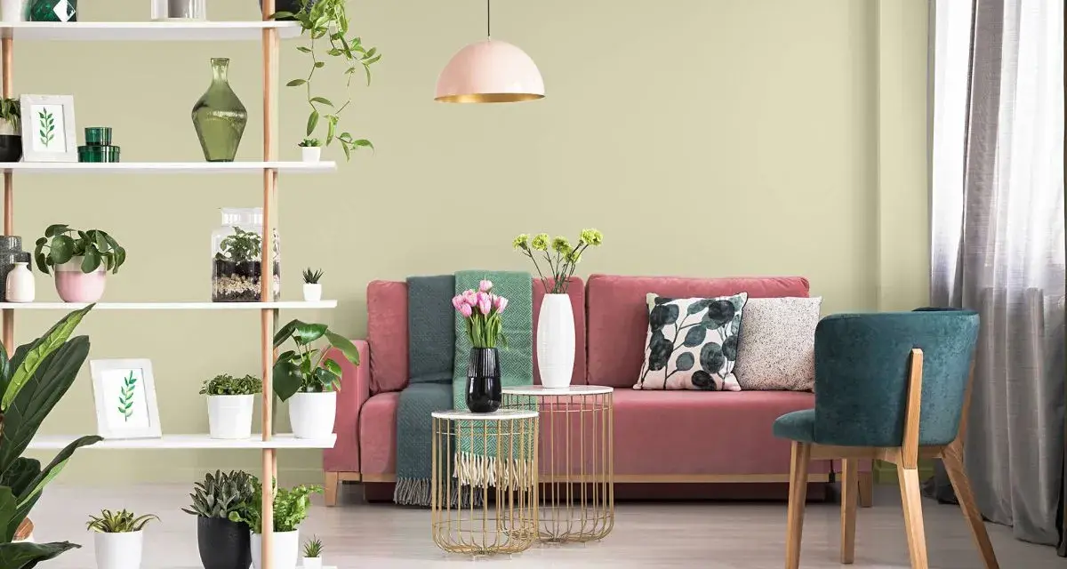 Salon z różową kanapą, zielonymi akcentami i roślinami. Ściany w subtelnym kolorze pistacjowym tworzą przytulną atmosferę.