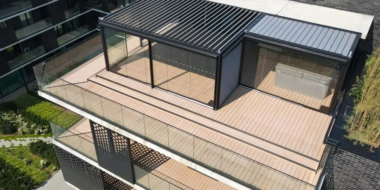 Nowoczesny taras na dachu z przeszklonym pawilonem i pergolą. Drewniana deska tarasowa i szklane balustrady tworzą elegancką przestrzeń.