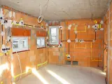 Rozprowadzona instalacja elektryczna w nowym budynku z cegły. Widoczne przewody, puszki i oznaczenia na ścianach.