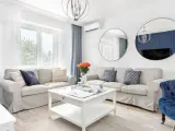 Jasny salon w stylu hampton z beżowymi sofami, niebieskimi akcentami i okrągłymi lustrami.