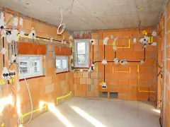 Rozprowadzona instalacja elektryczna w nowym budynku z cegły. Widoczne przewody, puszki i oznaczenia na ścianach.