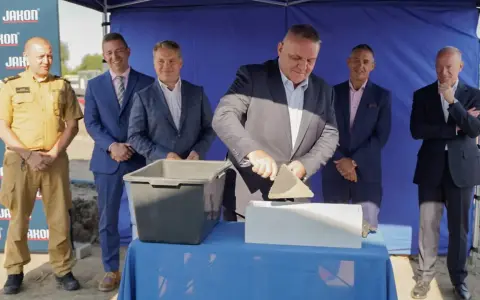 Uroczyste wmurowanie kamienia węgielnego. Mężczyzna w garniturze z kielnią w dłoni symbolicznie rozpoczyna budowę.