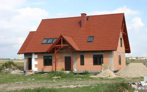 Dom w budowie z czerwonym dachem i oknami dachowymi. Wnętrze z potencjałem na wysoki, **sufit katedralny**.