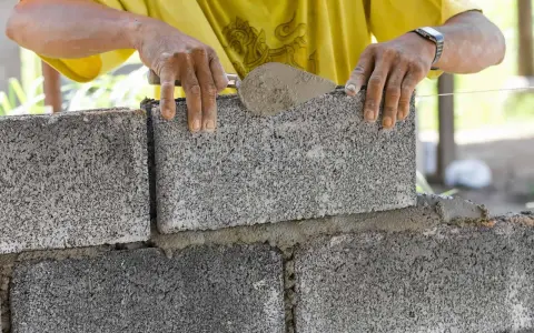 Ręce murarza układają bloczki betonowe fundamentowe, tworząc solidną podstawę.