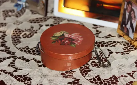 Okrągłe pudełko ozdobione techniką decoupage z motywem róż. Obok broszka i ramka ze zdjęciem.