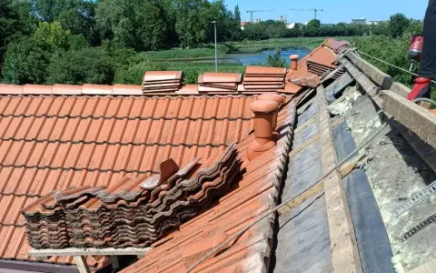 Trwa wymiana dachu. Stare dachówki są ułożone w stosy, a pod nimi widać izolację i drewniane elementy konstrukcji.