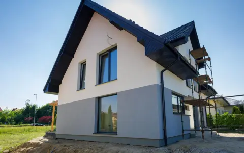 Nowy dom z dwukolorową elewacją, biało-szarą, to świetny pomysł na elewację domu. Widać rusztowania, co sugeruje trwające prace.