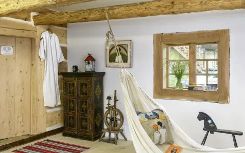 Wnętrze w stylu rustykalnym z drewnianymi belkami, hamakiem, zabytkową szafką i kołowrotkiem.