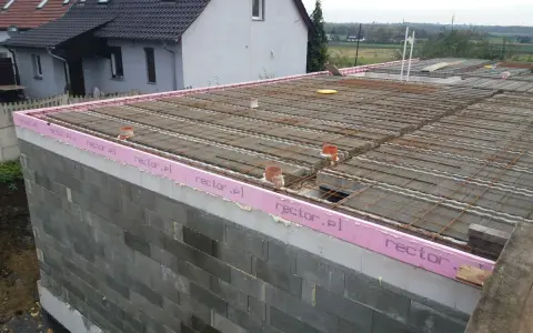 Budowa stropu zbrojonego, widoczne pustaki, różowa izolacja z napisem rector.pl i siatka zbrojeniowa.