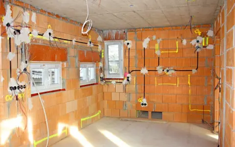 Rozprowadzona instalacja elektryczna w nowym budynku z cegły. Widoczne przewody, puszki i oznaczenia na ścianach.