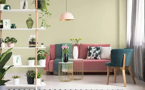 Salon z różową kanapą, zielonymi akcentami i roślinami. Ściany w subtelnym kolorze pistacjowym tworzą przytulną atmosferę.