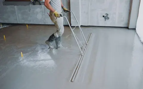 Robotnik wyrównuje świeżą wylewkę betonową. Sprawdź wylewka betonowa cena za m2 robocizny bez materiału.