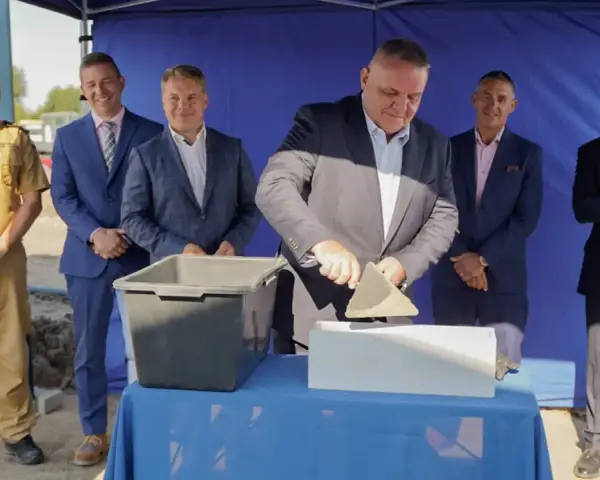 Uroczyste wmurowanie kamienia węgielnego. Mężczyzna w garniturze z kielnią w dłoni symbolicznie rozpoczyna budowę.