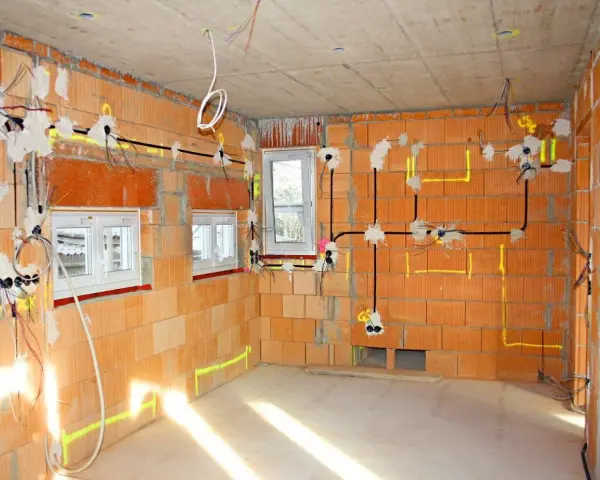 Rozprowadzona instalacja elektryczna w nowym budynku z cegły. Widoczne przewody, puszki i oznaczenia na ścianach.