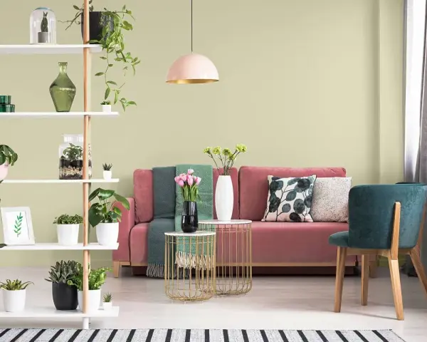 Salon z różową kanapą, zielonymi akcentami i roślinami. Ściany w subtelnym kolorze pistacjowym tworzą przytulną atmosferę.