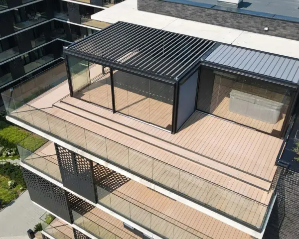 Nowoczesny taras na dachu z przeszklonym pawilonem i pergolą. Drewniana deska tarasowa i szklane balustrady tworzą elegancką przestrzeń.
