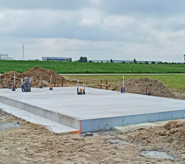 Solidny fundament czeka na budowę domu. Wokół piasek i zielone pola.