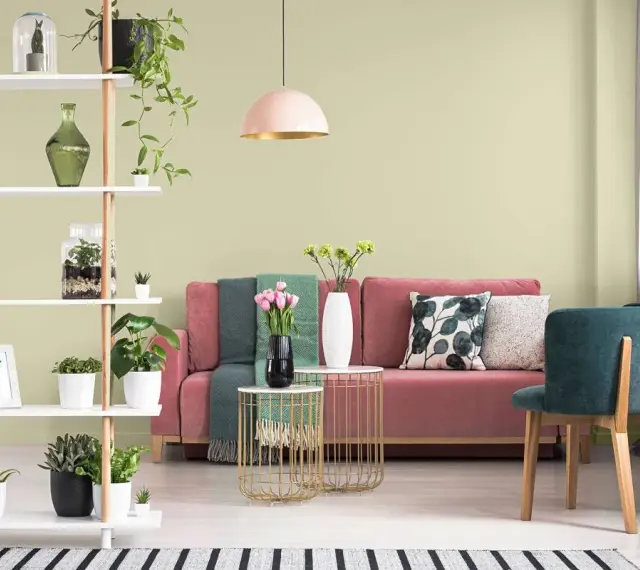 Salon z różową kanapą, zielonymi akcentami i roślinami. Ściany w subtelnym kolorze pistacjowym tworzą przytulną atmosferę.