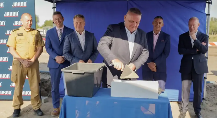 Uroczyste wmurowanie kamienia węgielnego. Mężczyzna w garniturze z kielnią w dłoni symbolicznie rozpoczyna budowę.