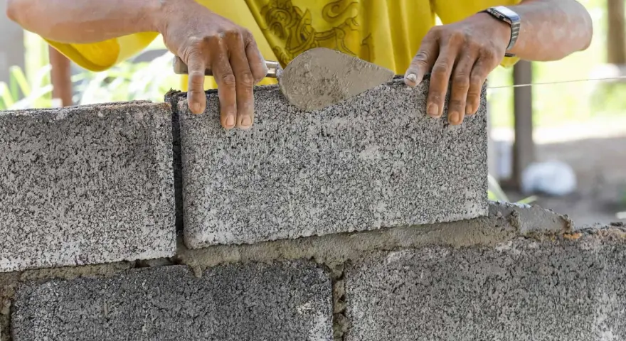 Ręce murarza układają bloczki betonowe fundamentowe, tworząc solidną podstawę.