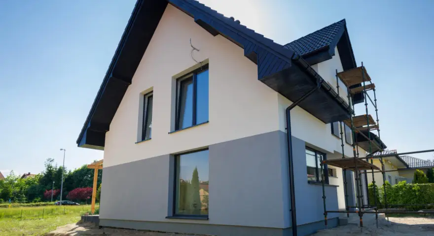 Nowy dom z dwukolorową elewacją, biało-szarą, to świetny pomysł na elewację domu. Widać rusztowania, co sugeruje trwające prace.