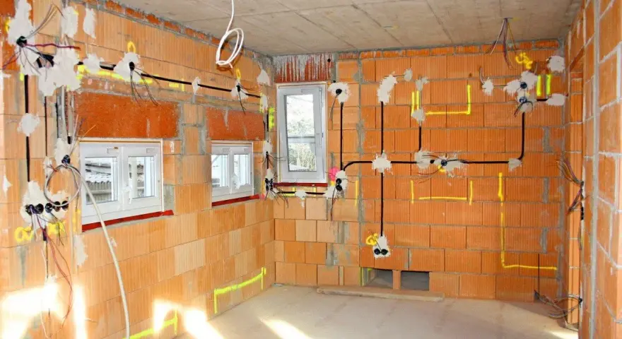 Rozprowadzona instalacja elektryczna w nowym budynku z cegły. Widoczne przewody, puszki i oznaczenia na ścianach.
