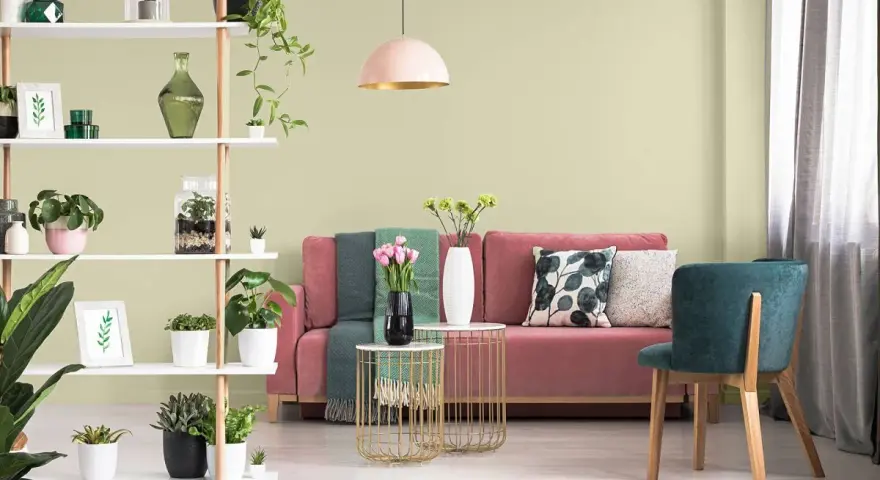Salon z różową kanapą, zielonymi akcentami i roślinami. Ściany w subtelnym kolorze pistacjowym tworzą przytulną atmosferę.