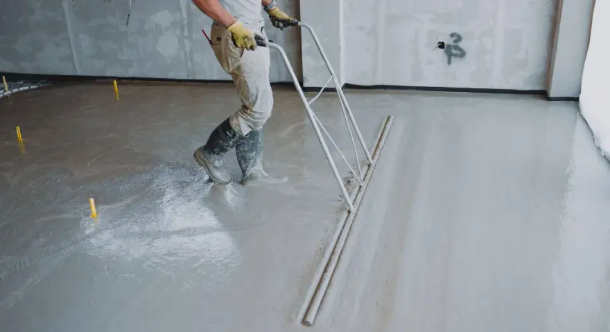 Robotnik wyrównuje świeżą wylewkę betonową. Sprawdź wylewka betonowa cena za m2 robocizny bez materiału.