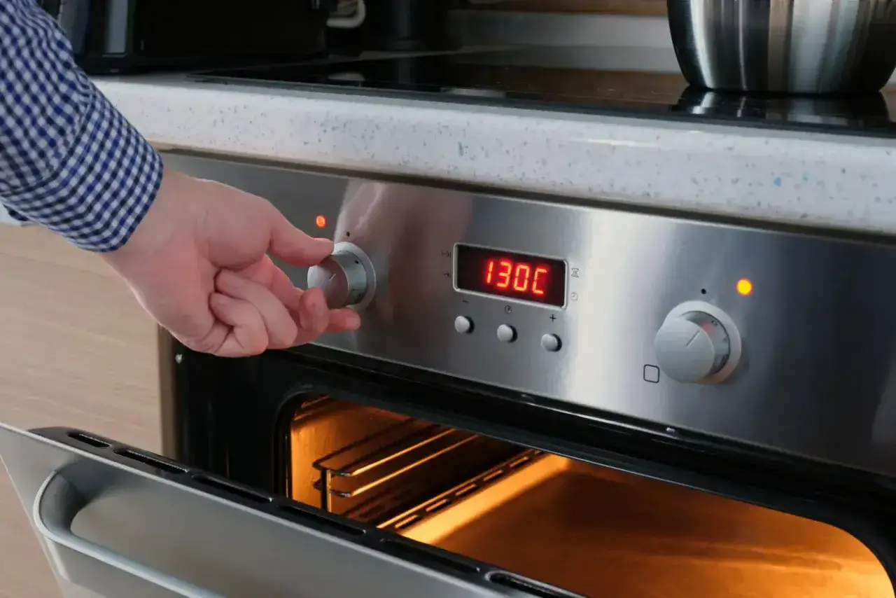 Ręka kręci pokrętłem piekarnika ustawiając 130°C. To pierwszy krok, jak wyparzyć słoiki w piekarniku.