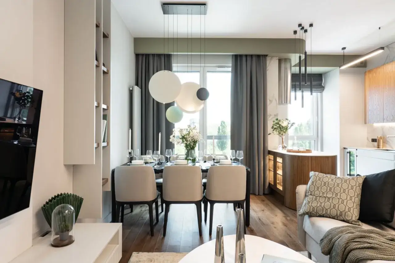 Elegancka jadalnia z oknem i zasłonami w kolorze pistacjowym. Stół nakryty do kolacji, nowoczesne krzesła, designerska lampa.