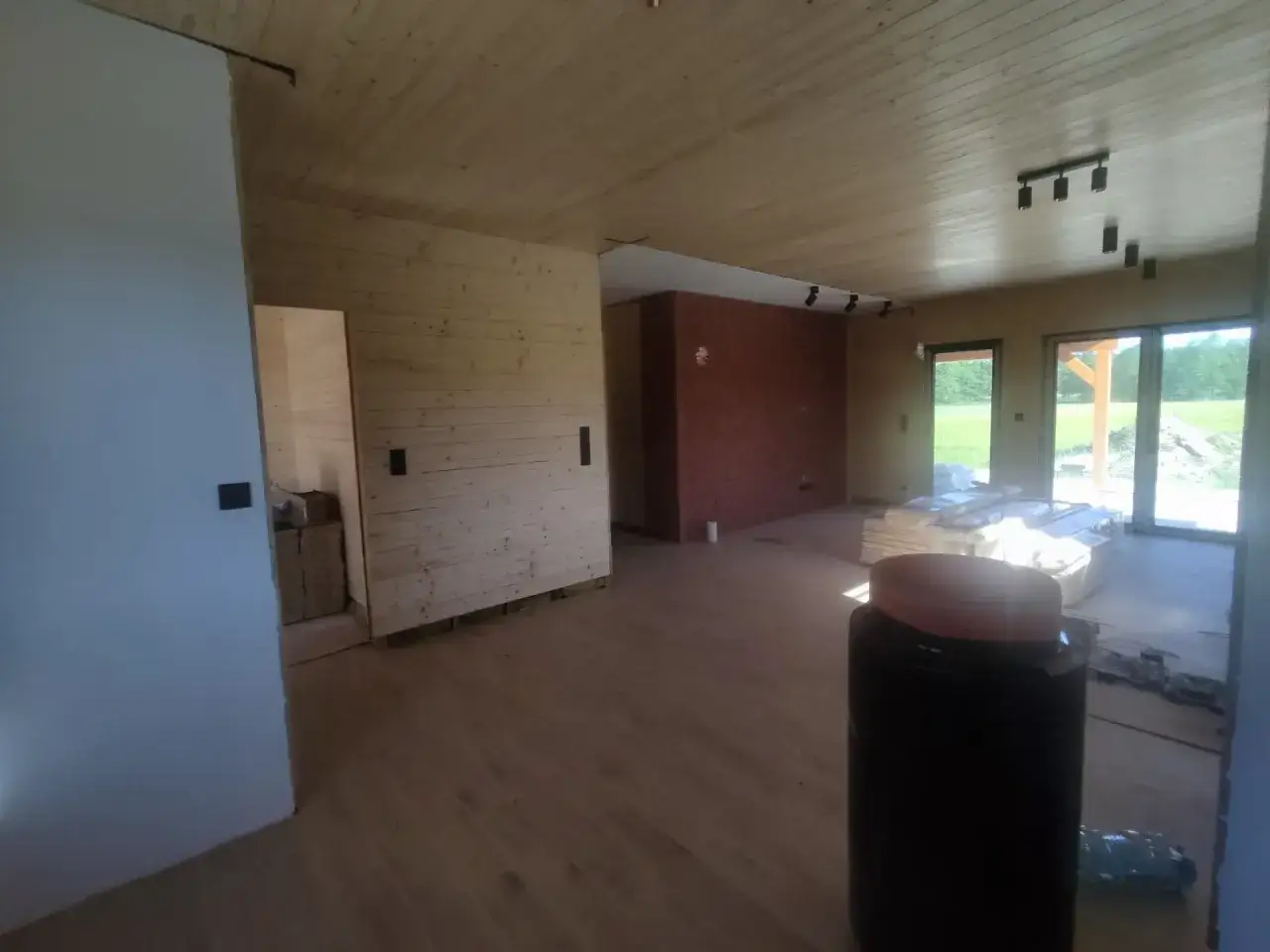 Wnętrze domu kanadyjskiego w trakcie budowy. Drewniane ściany i sufit, podłoga z płytek, ceglana ściana działowa.