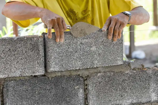 Ręce murarza układają bloczki betonowe fundamentowe, tworząc solidną podstawę.