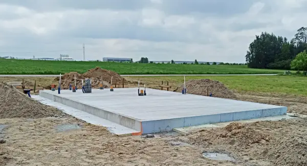 Solidny fundament czeka na budowę domu. Wokół piasek i zielone pola.