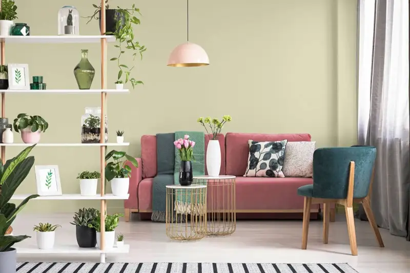 Salon z różową kanapą, zielonymi akcentami i roślinami. Ściany w subtelnym kolorze pistacjowym tworzą przytulną atmosferę.